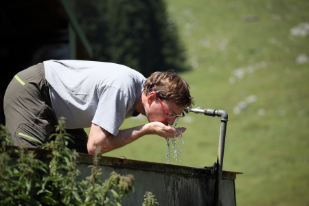 a man is drinking from afountain in the mountainsの写真素材