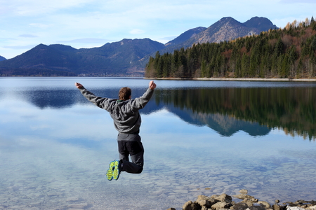 man is jumping for fun with lake in background