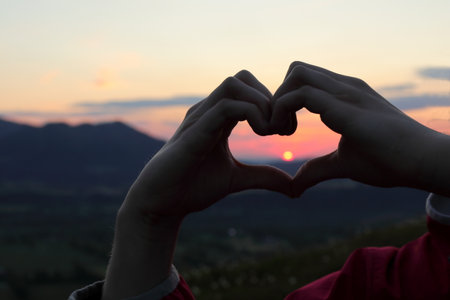 two kid hands are forming a heart at sundownの写真素材