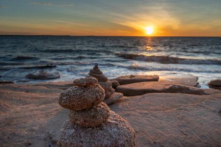 A Serene and Beautiful Sunset Over the Vast Ocean Featuring Stacked Stones Along the Shorelineの写真素材