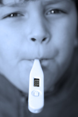Close crop image of a boy with a digital thermometer in his mouth,focus on the read out,toned blue to emphasise winter 'cold'の写真素材
