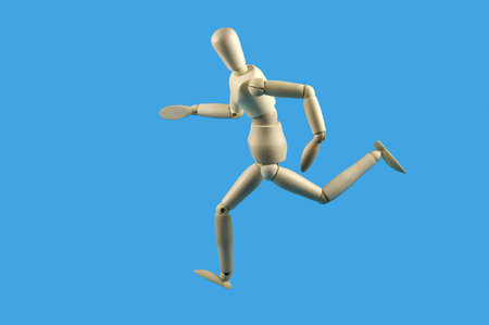 Wooden mannequin in a running pose, isolated against a sky blue backgroundの写真素材