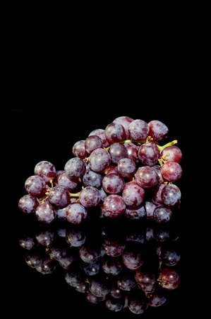 Bunch of red grapes on a black background with reflectionの写真素材