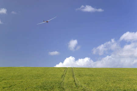 Glider flying over a landscape of green field and blue skyの写真素材