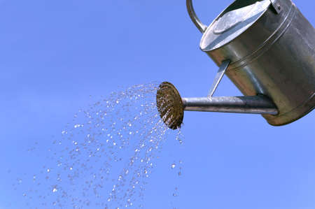 Water pouring from a watering can against a blue sky.の写真素材