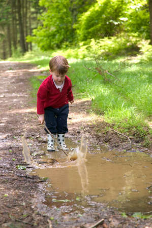Toddler splashing in a muddy puddle with his stick.の写真素材