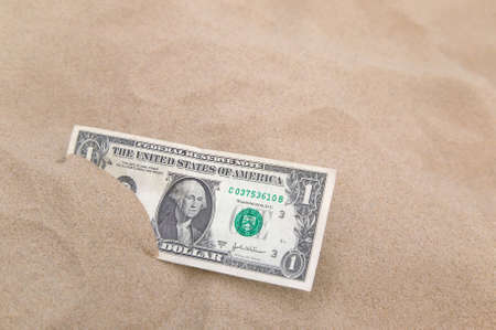 One US dollar partly buried in sand, focus on the note.の写真素材