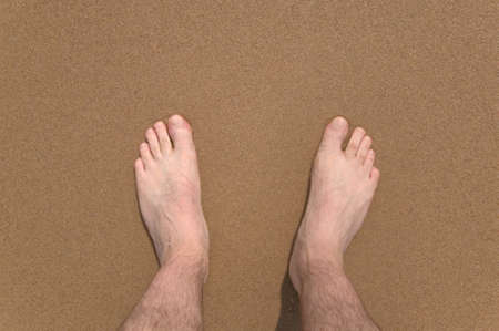 Downward view of a man's legs and feet at the beach.