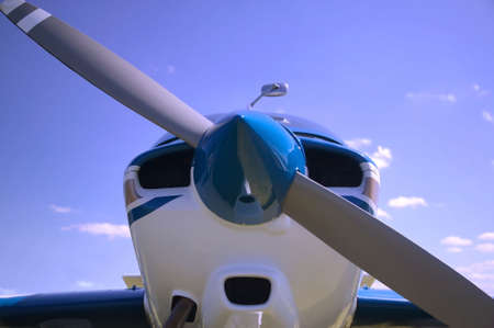 Close up of a light aircrafts nose cone against a blue cloudy sky.