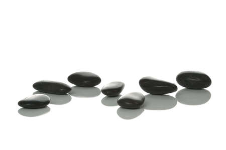 Seven black pebbles with reflections on a white background, high key shot.の写真素材
