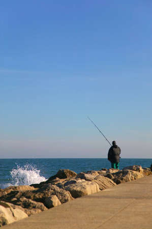 An angler line fishing from some rocks.の写真素材