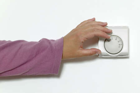 Womans hand turning down the temperature on a room thermostat.の写真素材