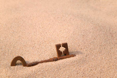 A rusty old key part buried in sand.の写真素材