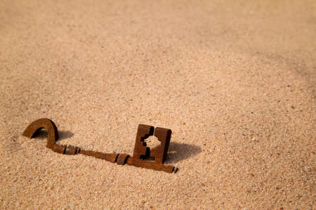 A rusty old key buried in the sandの写真素材