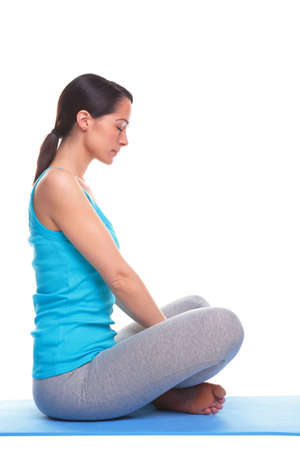 A brunette woman sat in a relaxed lotus position on a yoga mat, isolated on a white background.の写真素材