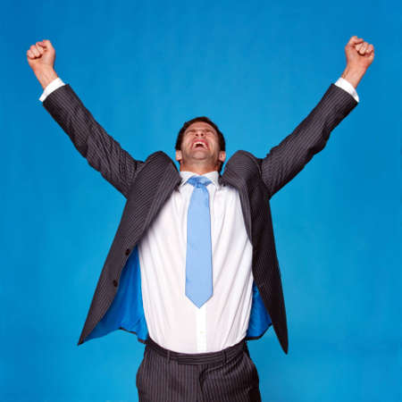 Businessman celebrating with his arms raised in the air, blue background.の写真素材
