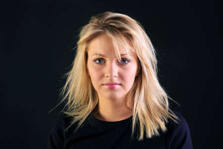 Portrait of a beautiful blonde haired woman with blue eyes on a black background.の写真素材