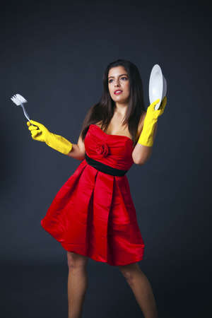 A woman in a red evening dress wearing rubber gloves and holding a dish and brush, glamorous...