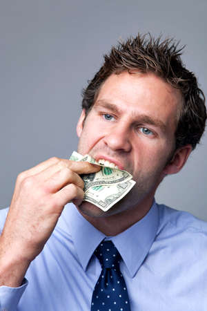 A businessman stuffing bank notes in his mouth.の写真素材
