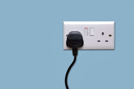 Double electrical power socket and single plug switched on, blue background.の写真素材