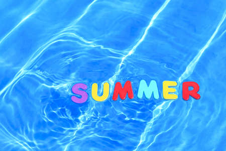 Photo of the word SUMMER made from foam letters floating in water on the surface of a swimming pool.の写真素材