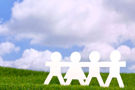 Concept image of paper people holding hands in a field with a blue sky background.の写真素材