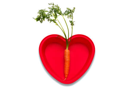 Conceptual photo of a carrot in a heart shaped dish to represent a love of the vegetable, isolated on a white background with clipping path. Part of a series.の写真素材