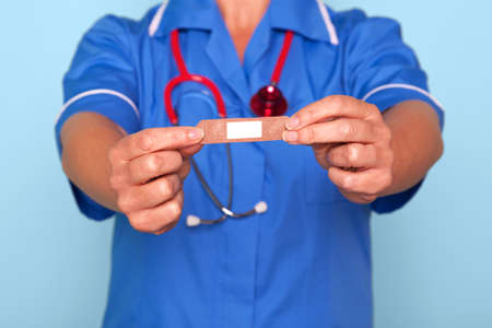 Photo of a nurse in uniform holding a bandaid sticky plaster towards camera.の写真素材