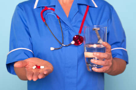 Photo of a nurse in uniform holding some pills and a glass of waterの写真素材