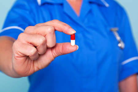 Photo of a nurse in uniform holding a pill towards camera, focus is on the pill.の写真素材