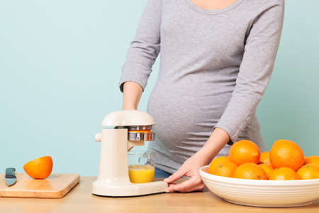 Photo of a 32 week pregnant woman in her kitchen preparing freshly squeezed orange juice.