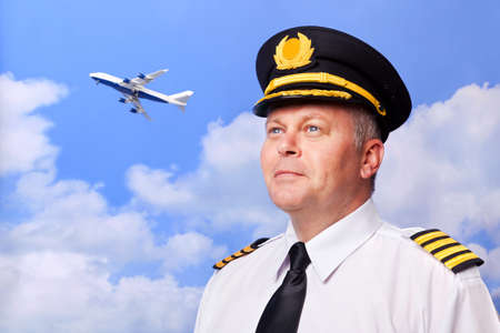 Photo of an airline pilot wearing the four bar Captains epaulettes, shot against a sky background with jumbo jet taking off in the distance.の写真素材