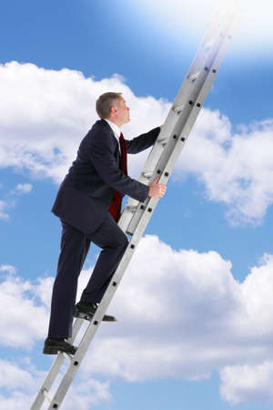 Concept photo of a businessman climbing a ladder into the sky looking up into the light.の写真素材