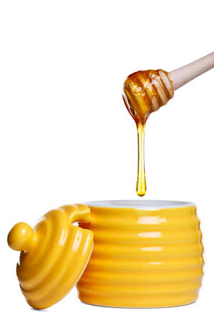 Yellow beehive shaped honey pot with dripping dipper held above, isolated on a white background. の写真素材