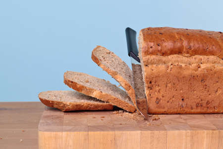 Wholemeal loaf of bread being sliced with a knife.