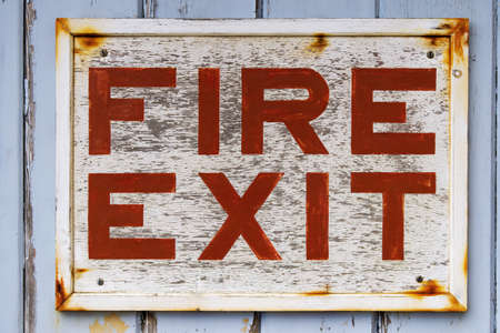 Photo of an old weathered FIRE EXIT sign on a blue door with peeling paint.の写真素材