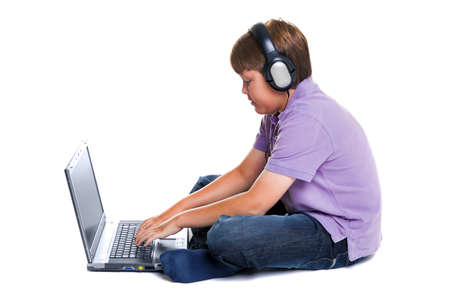 Photo of an 11 year old school boy wearing headphones sitting with a laptop computer, isolated on a...