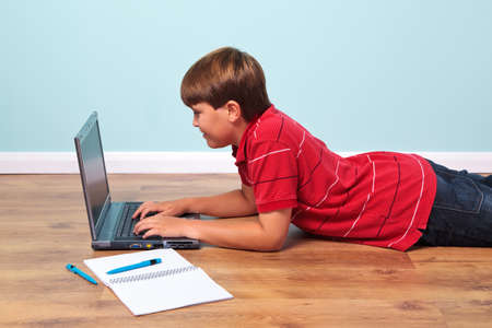 Photo of a boy lying on the floor typing on his laptop computerの写真素材
