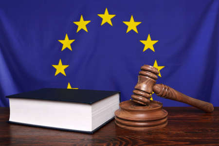 Still life photo of a gavel, block and law book on a judges bench with the European Union flag behind.の写真素材