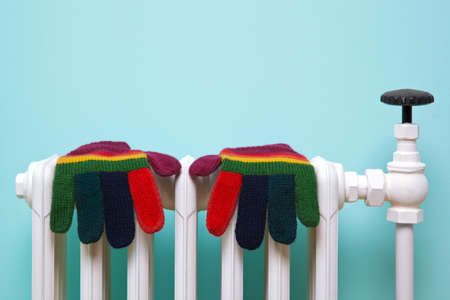 Photo of a pair of hand knitted striped woolen gloves drying on an old traditional cast iron radiator. の写真素材