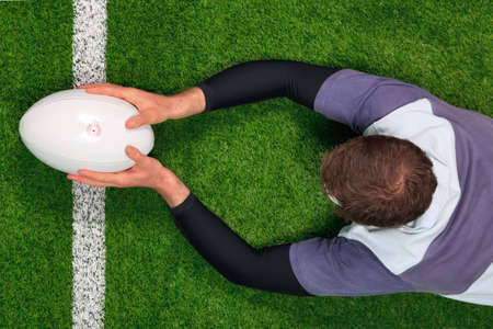 Overhead photo of a rugby player diving over the line to score a try with both hands holding the ball.の写真素材