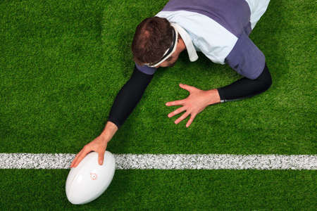 Overhead photo of a rugby player stretching over the line to score a try with one hand on the ball.の写真素材