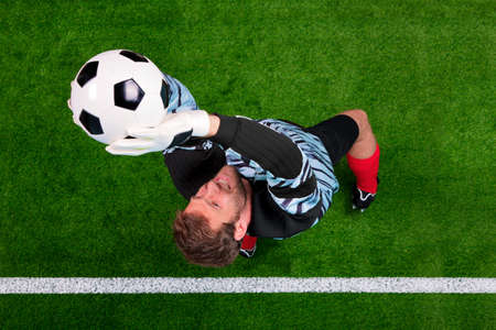 Overhead photo of a football goalkeeper jumping in the air saving the ball on the line. Focus point is on his face.の写真素材