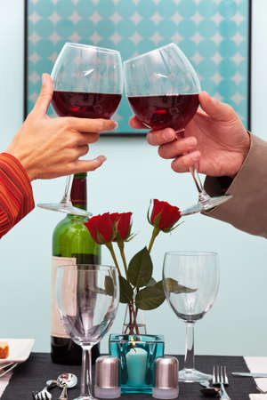 Photo of a couples hands toasting their glasses of red wine over the table in a restaurantの写真素材
