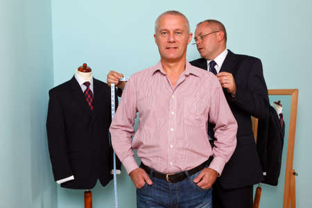 Photo of a tailor measuring the shoulder width of a man for the fitting of a new bespoke suitの写真素材