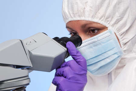 Photo of a biochemist looking through a stereo optical laboratory microscope at a specimen on a slide.の写真素材