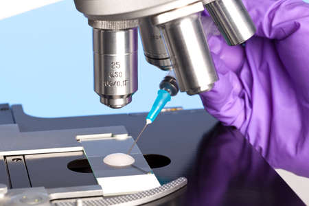 Photo of a sperm sample on a microscope slide with a syringe being used to extract an embryology specimen for analysis.の写真素材