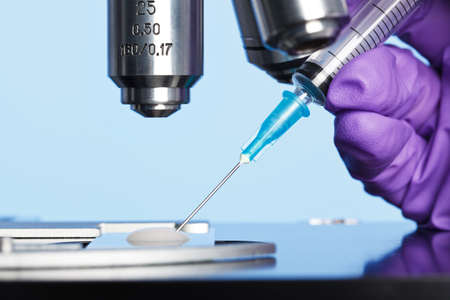 Photo of a sperm sample on a microscope slide with a syringe being used to extract an embryology specimen for analysis.の写真素材