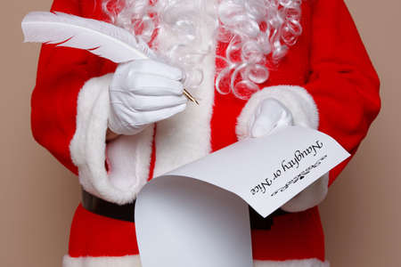 Santa Claus holding a quill pen whilst checking the naughty or nice list.の写真素材