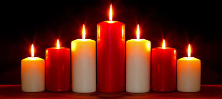 Still life photo of red and white church candles arranged in an arch burning with bright flames against a black background.の写真素材